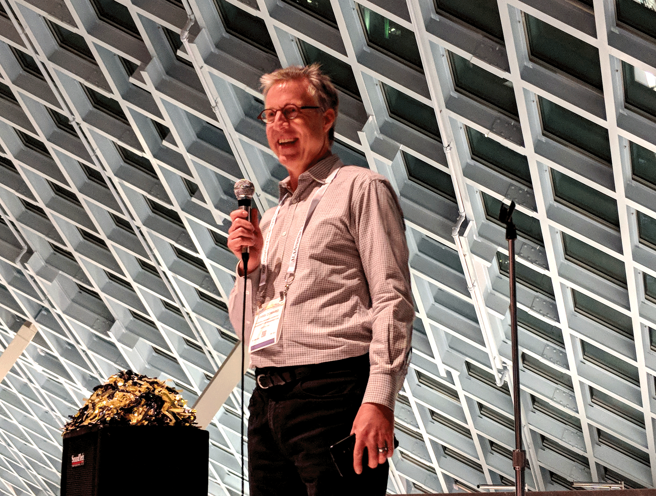 Chris Coward smiling and holding a microphone.