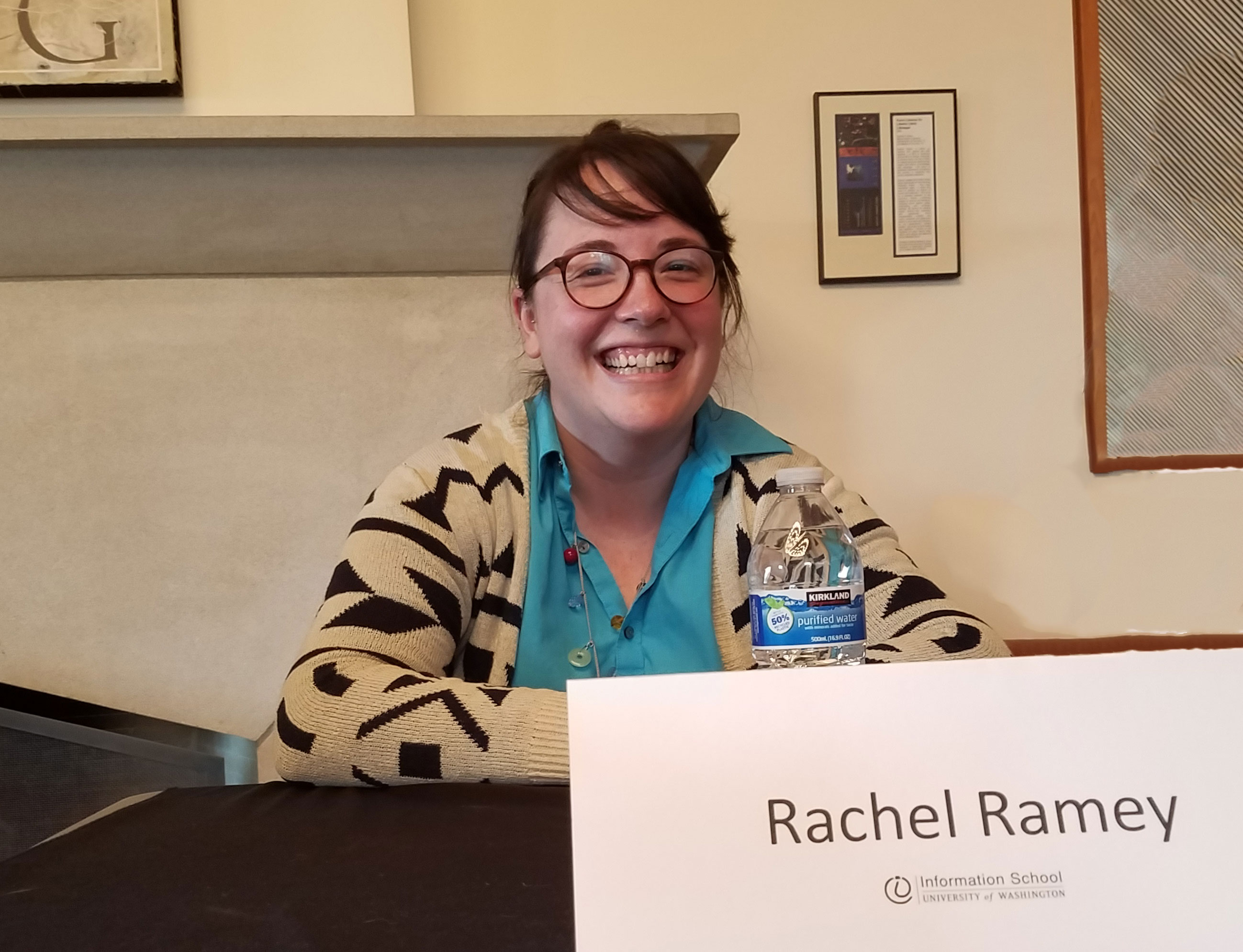 Smiling, young woman wearing glasses seated at a table with a name tag that reads Rachel Ramey.