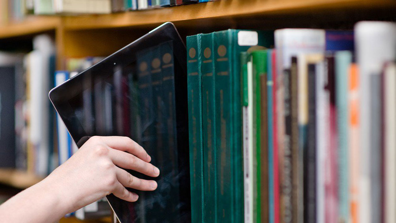 Digital tablet being pulled from a row of books