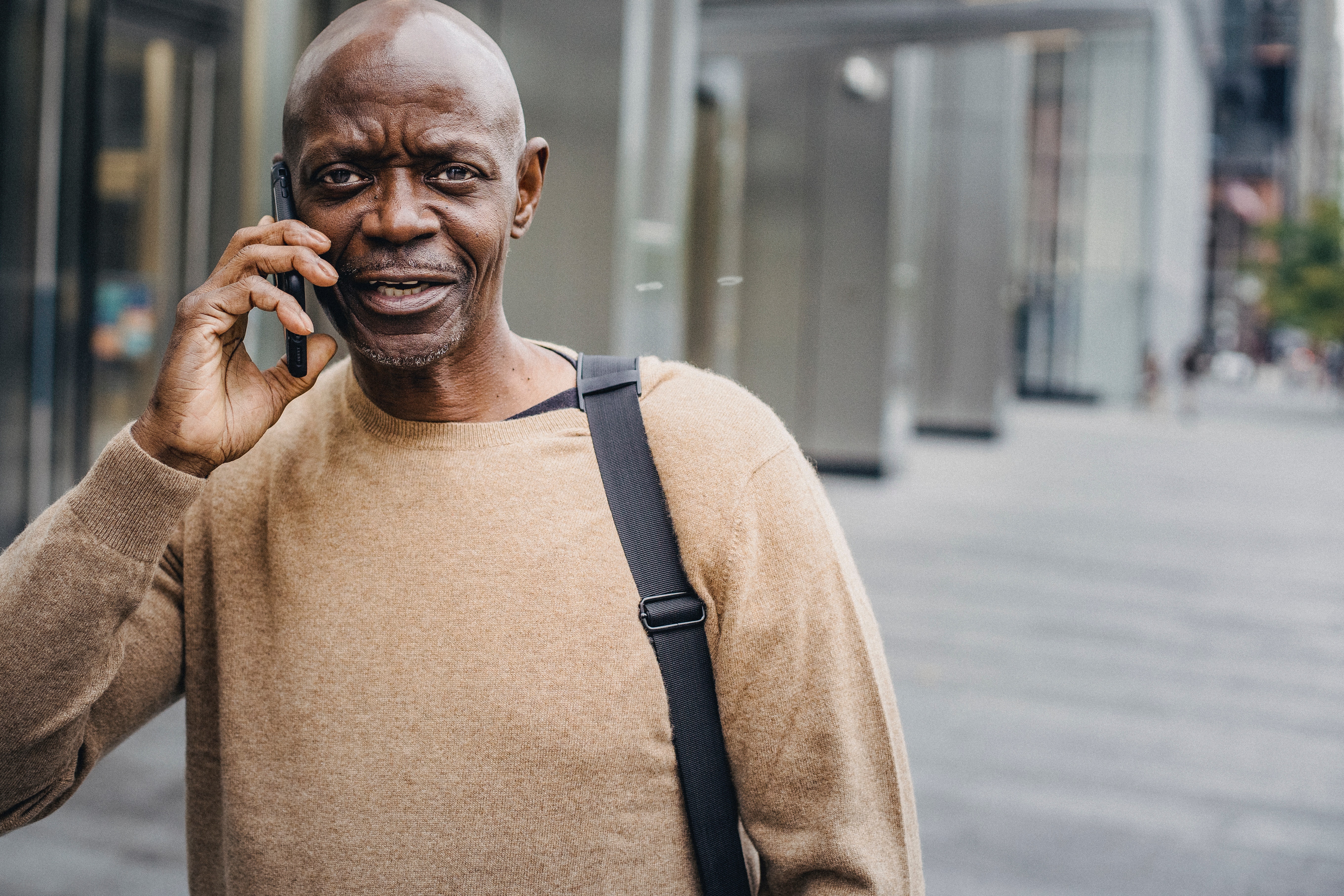 A man wearing a tan sweater talking on his cell phone outside.